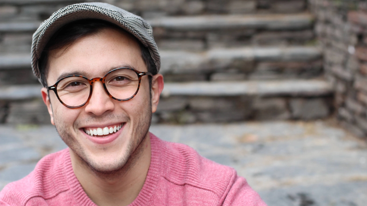 Ein junger Mann mit Mütze und Brille lächelt in die Kamera.