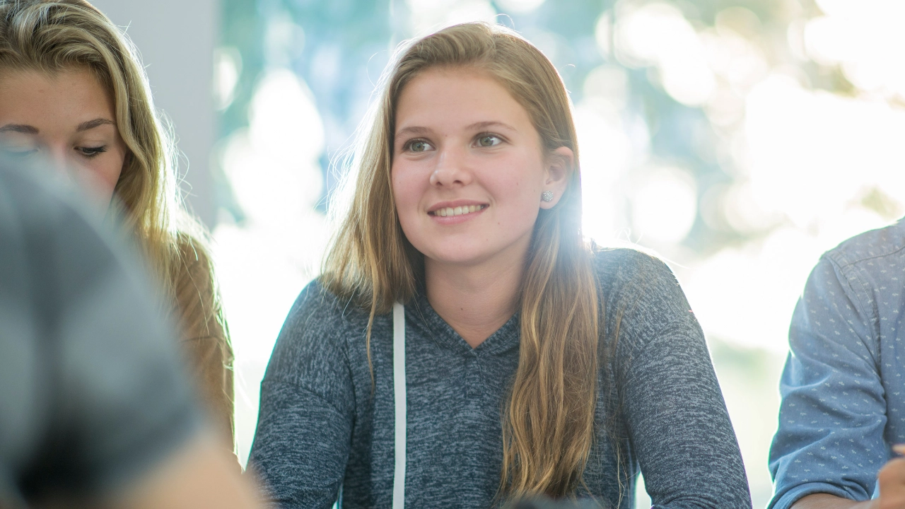 Ein Blondes Mädchen schaut lächelnd nach vorne während eines Seminars.