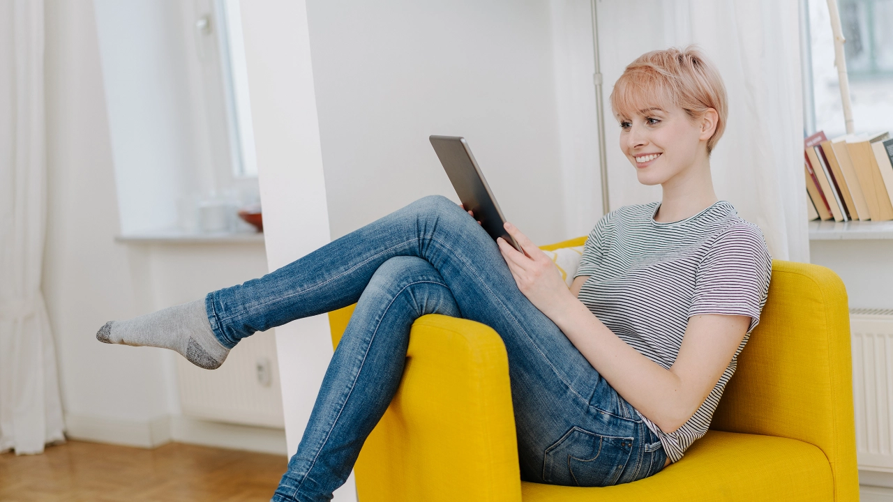 Junge Frau sitzt im Sessel und schaut auf ihr Tablet