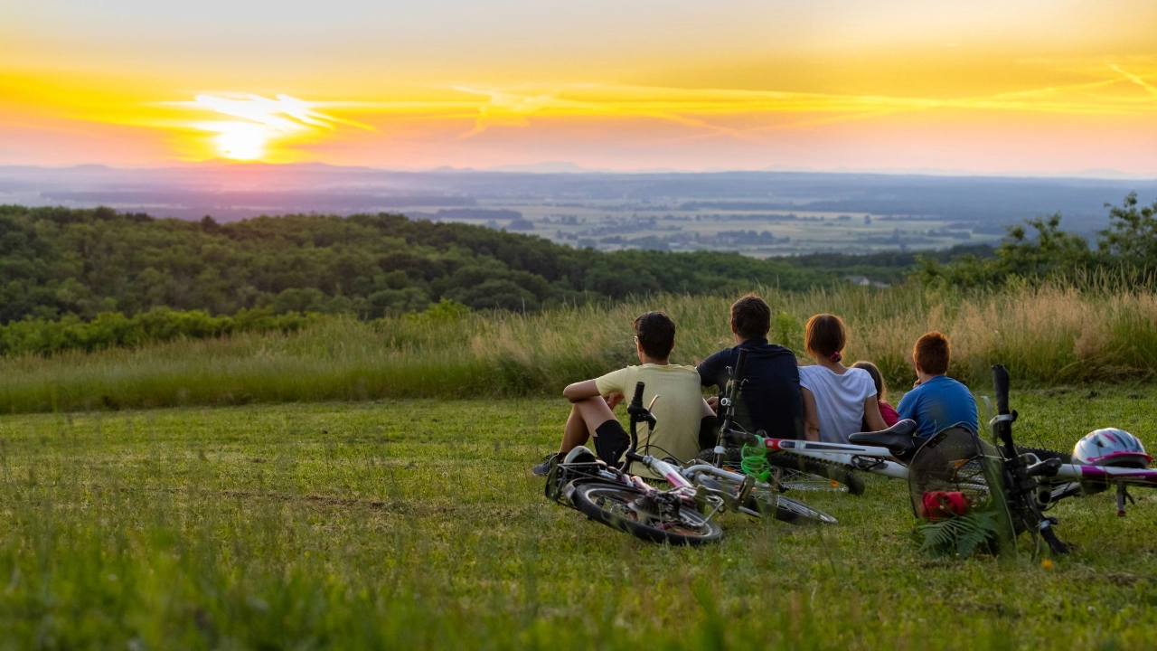 Familie, die nach einer Radtour auf einem Hügel sitzt und den Sonnenuntergang betrachtet 