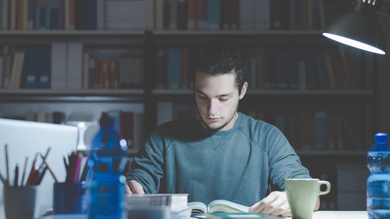 Ein junger Mann sitzt an einem Schreibtisch und schaut in ein Buch.