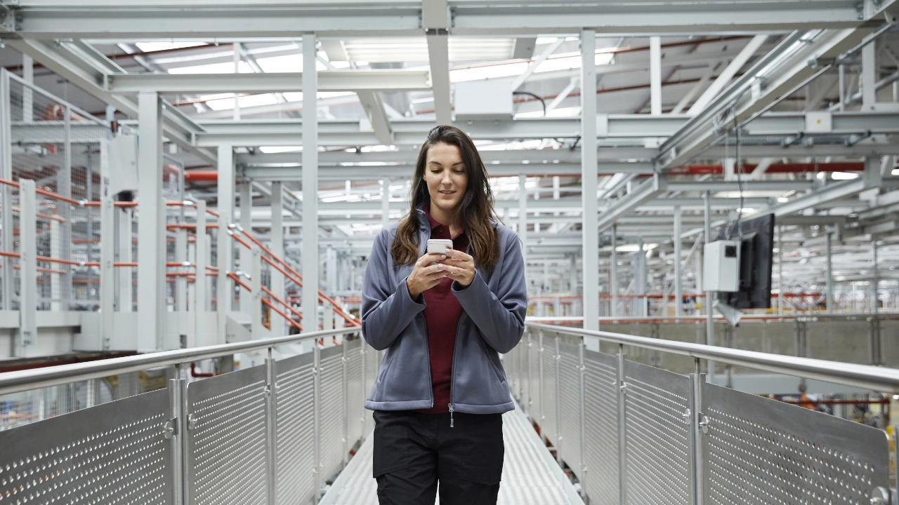Eine junge Frau in Arbeitskleidung blickt auf ein Smartphone.