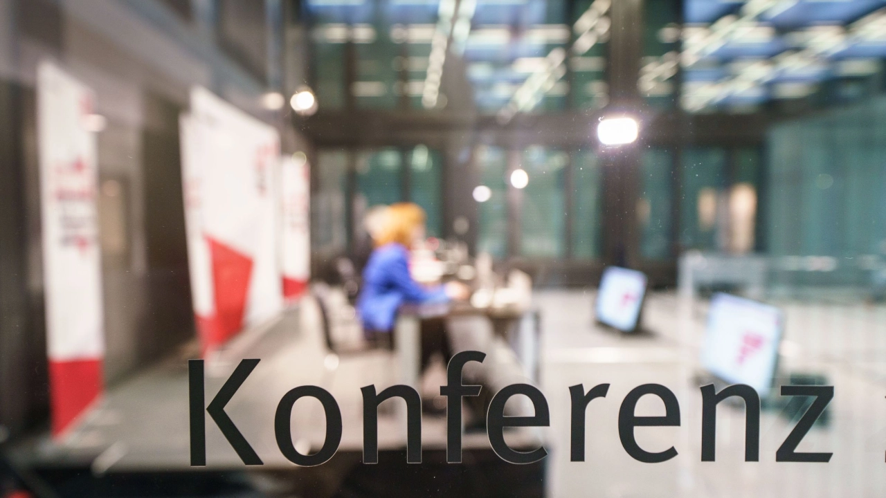 Glasscheibe mit der Aufschrift "Konferenz", dahinter unscharf ein Konferenzraum