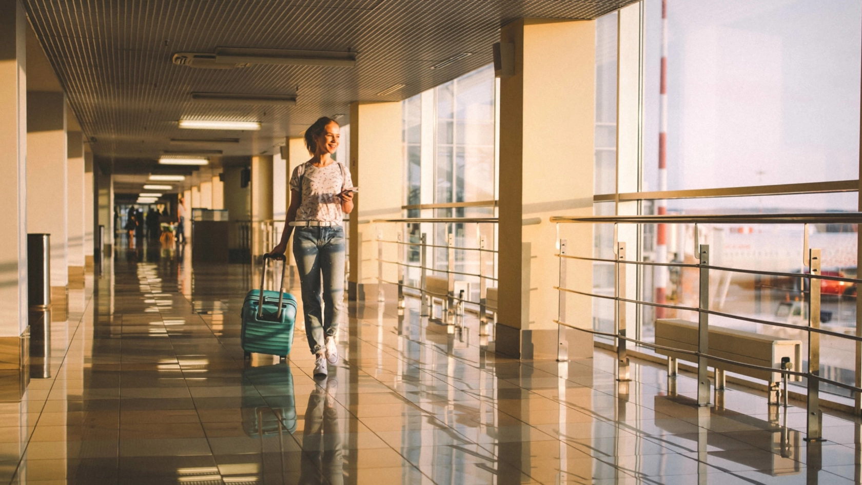 Eine junge Frau mit Rollkoffer geht durch einen Flur in einem Flughafen.