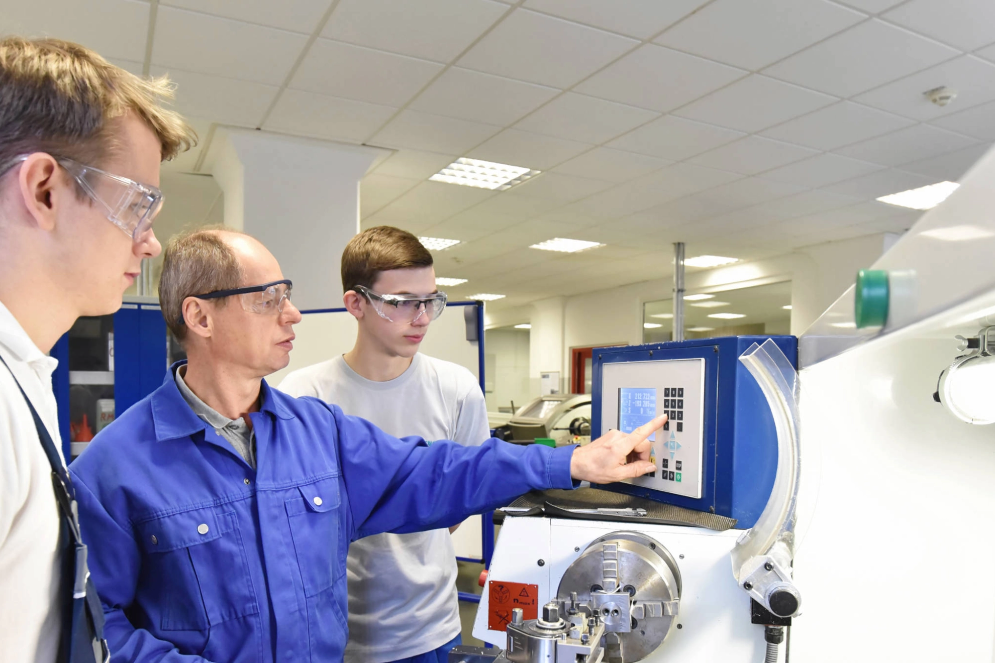 Junge Auszubildende werden an einer CNC-Maschine trainiert.