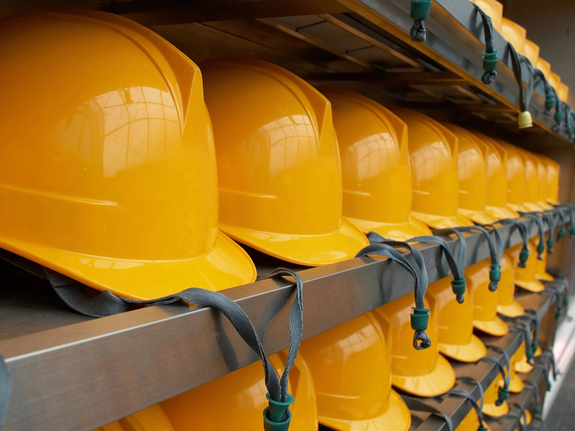 Viele gelbe Schutzhelme liegen in mehreren Reihen neben- und übereinander in einem Regal als Symbol für Arbeitssicherheit.