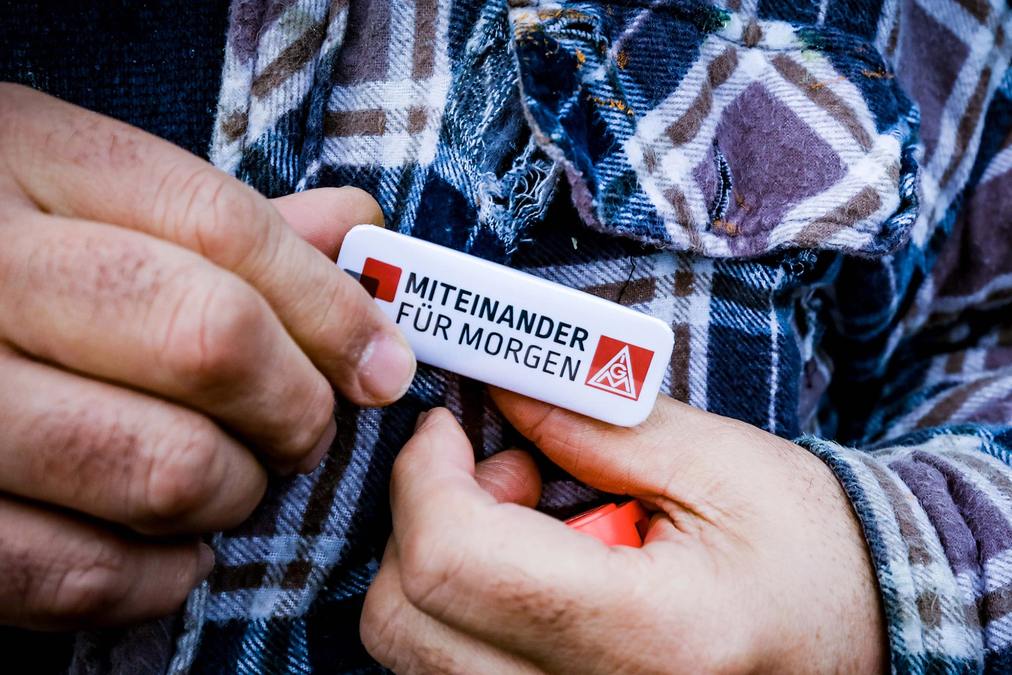 ann steckt IG-Metall-Pin an sein kariertes Hemd.