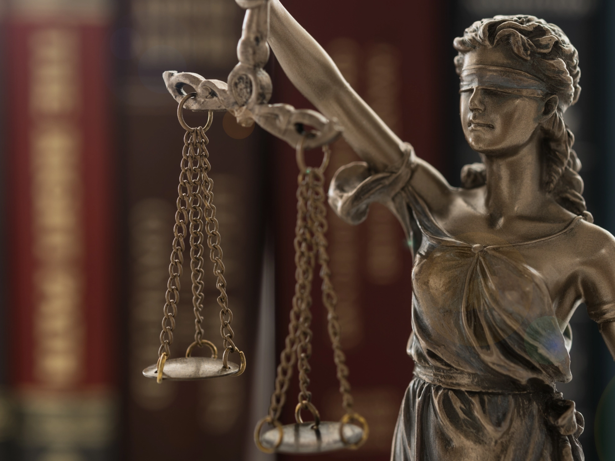 Bronzestatue von Justizia mit Waage in der Hand vor unscharfen Gesetzbüchern im Hintergrund