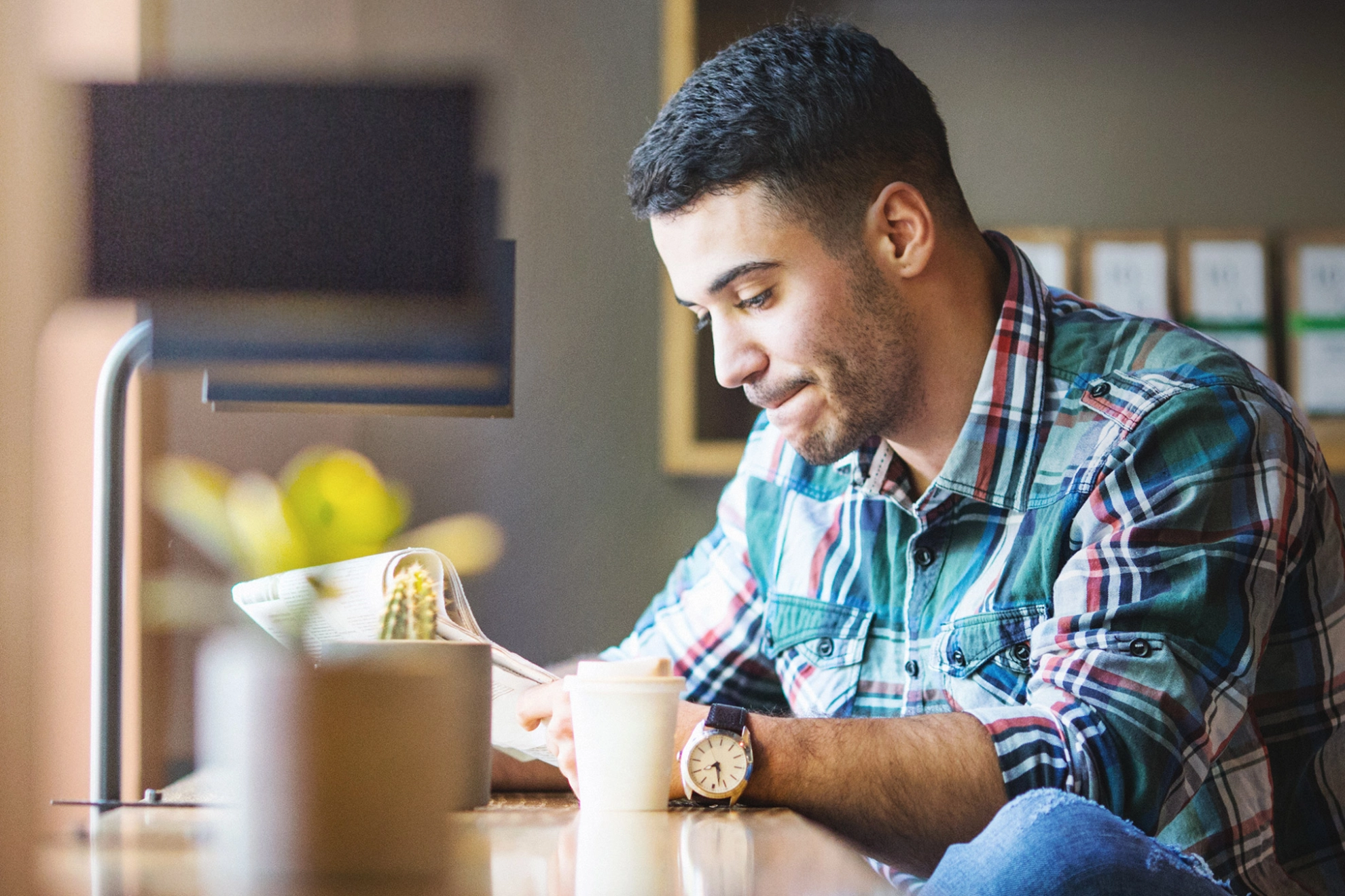 Ein junger Mann liest Zeitung und trinkt dabei Kaffee.