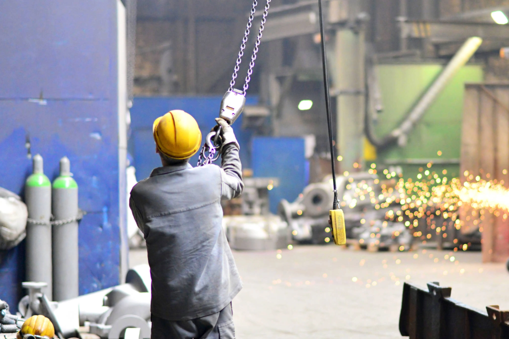 Ein Mann mit Schutzhelm hält eine Metallkette, die an einem Kran hängt.
