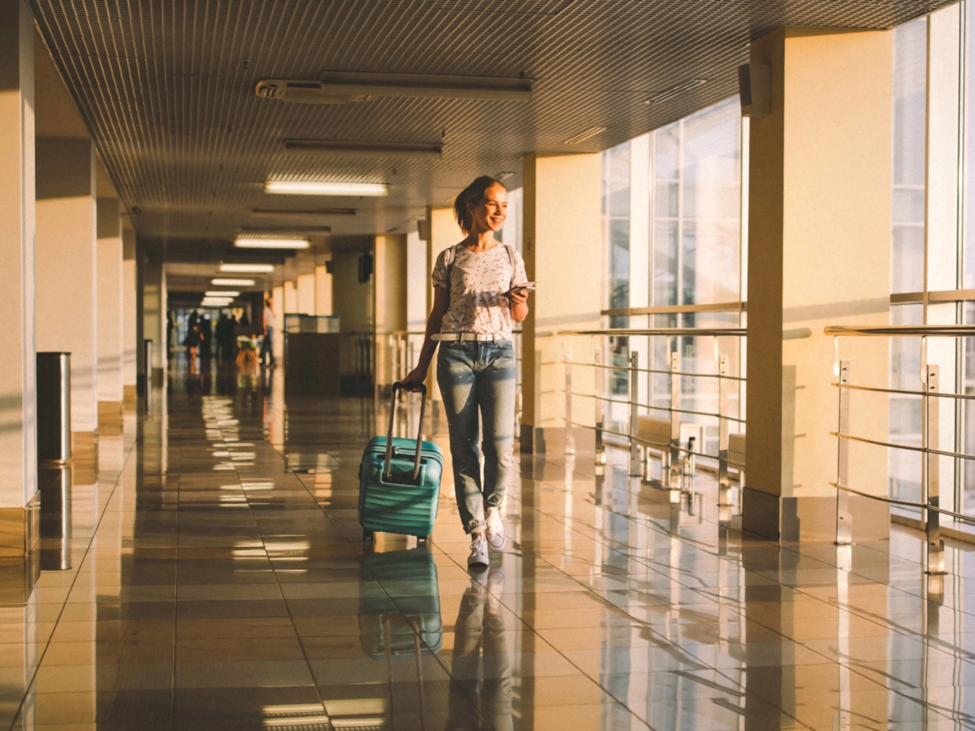 Eine junge Frau mit Rollkoffer geht durch einen Flur in einem Flughafen.