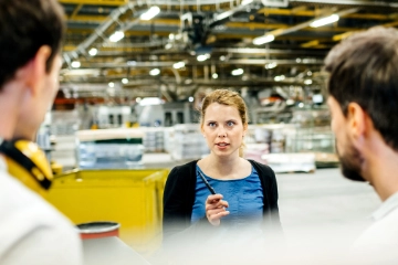 Eine Frau spricht mit zwei Männern an einer Produktionslinie.