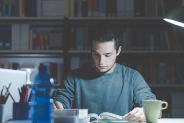 Ein junger Mann sitzt an einem Schreibtisch und schaut in ein Buch.