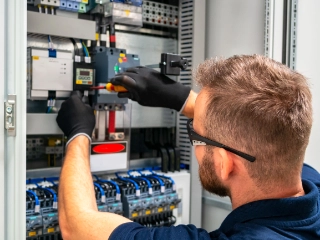 Ein Elektroniker mit Schutzbrille und Handschuhen arbeitet an einem Schaltschrank