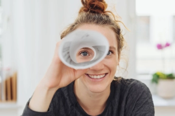 Eine junge Frau blickt durch ein gerolltes Blatt Papier.