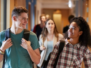 Eine Studentin und ein Student gehen gemeinsam über einen Korridor in einem Universitätsgebäude.