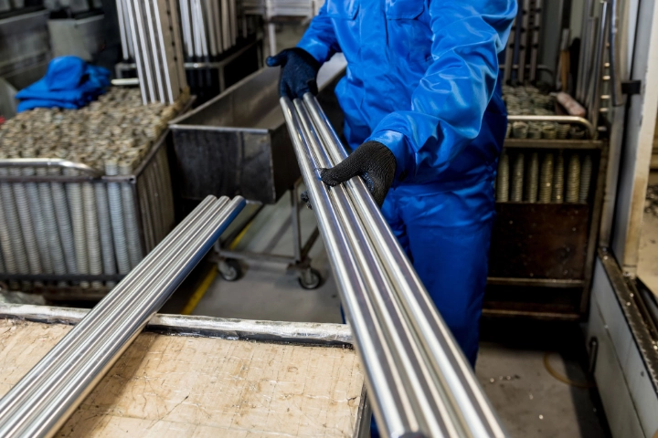 Ein Beschäftigter in einer Werkshalle hält Metallrohre in den Händen