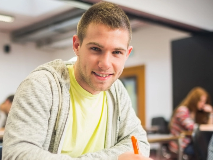 Student sitzt an einem Tisch im Seminarraum und macht sich Notizen.